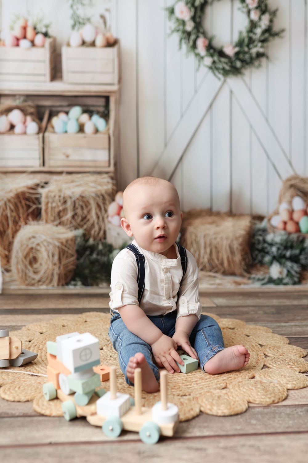 Spring themed baby portrait setup with wooden toy train, hay bales, and floral decor in rustic farmhouse style setting.