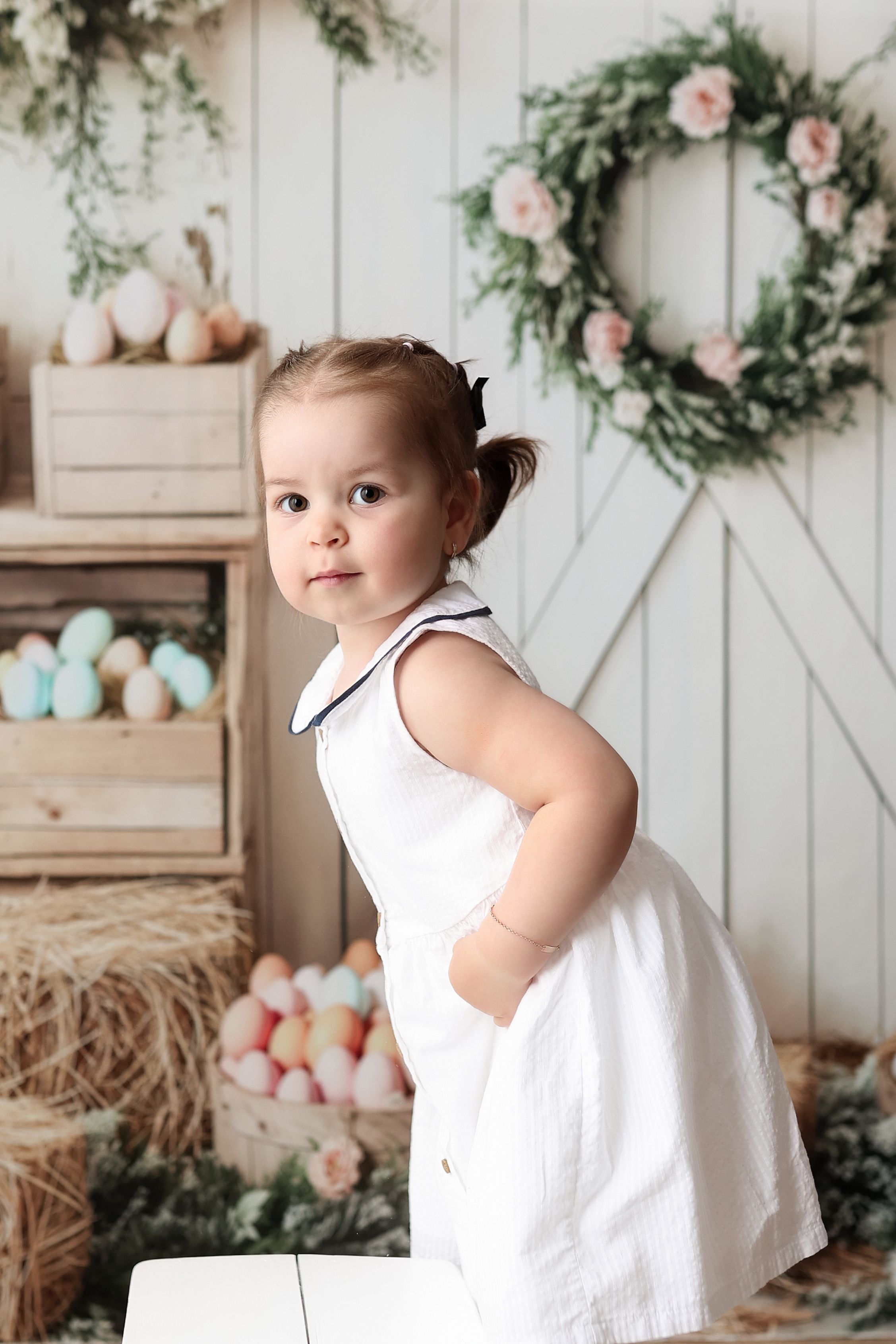 A white rustic spring scene with pastel eggs, a floral wreath, and Easter decor against a white wooden barn door backdrop.