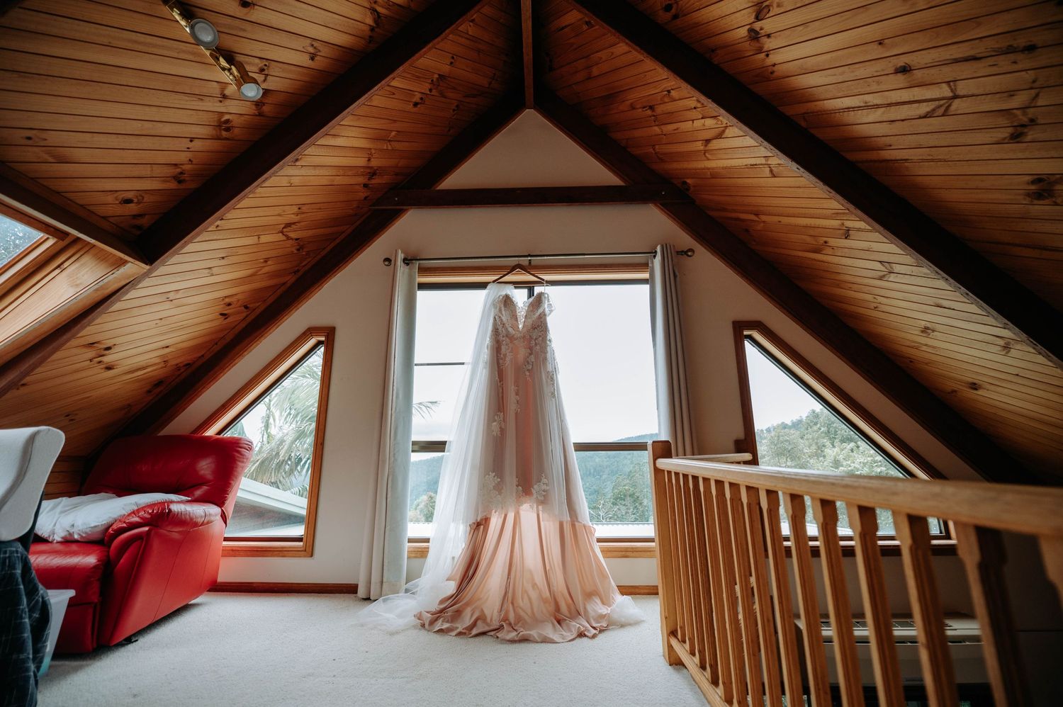 Blush wedding dress hanging in a rustic A-frame cabin loft with natural lighting.