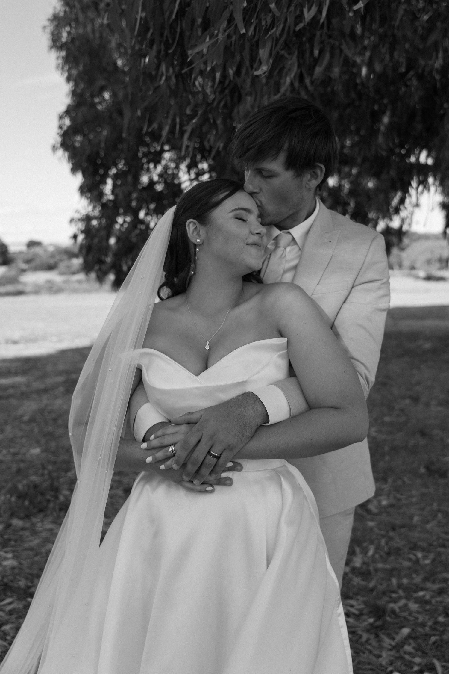 A tender wedding moment captured in black and white as a couple embraces outdoors.