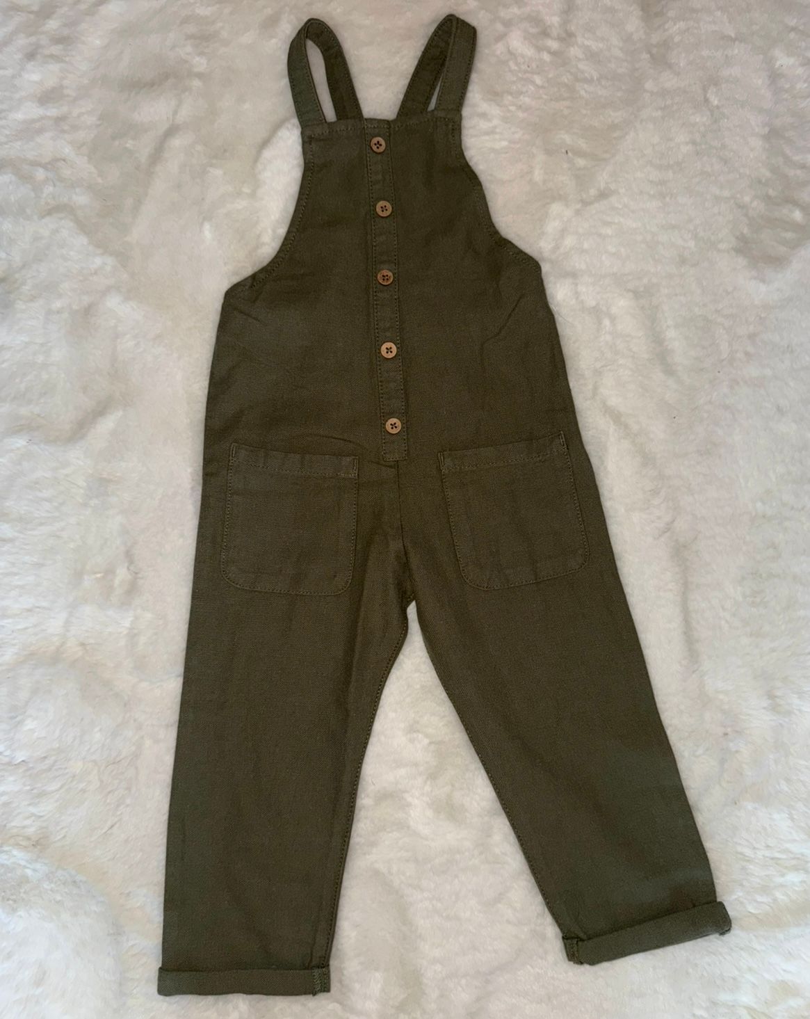 Dark olive green overalls laid flat on a white surface showing different folding positions.