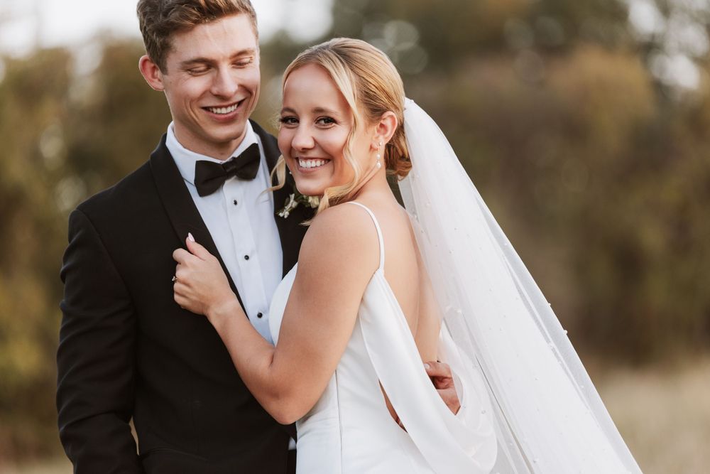 A romantic wedding portrait of a newlywed couple embracing outdoors during golden hour.
