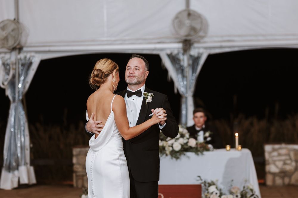 A couple shares their first dance in an elegantly decorated reception tent with soft lighting.