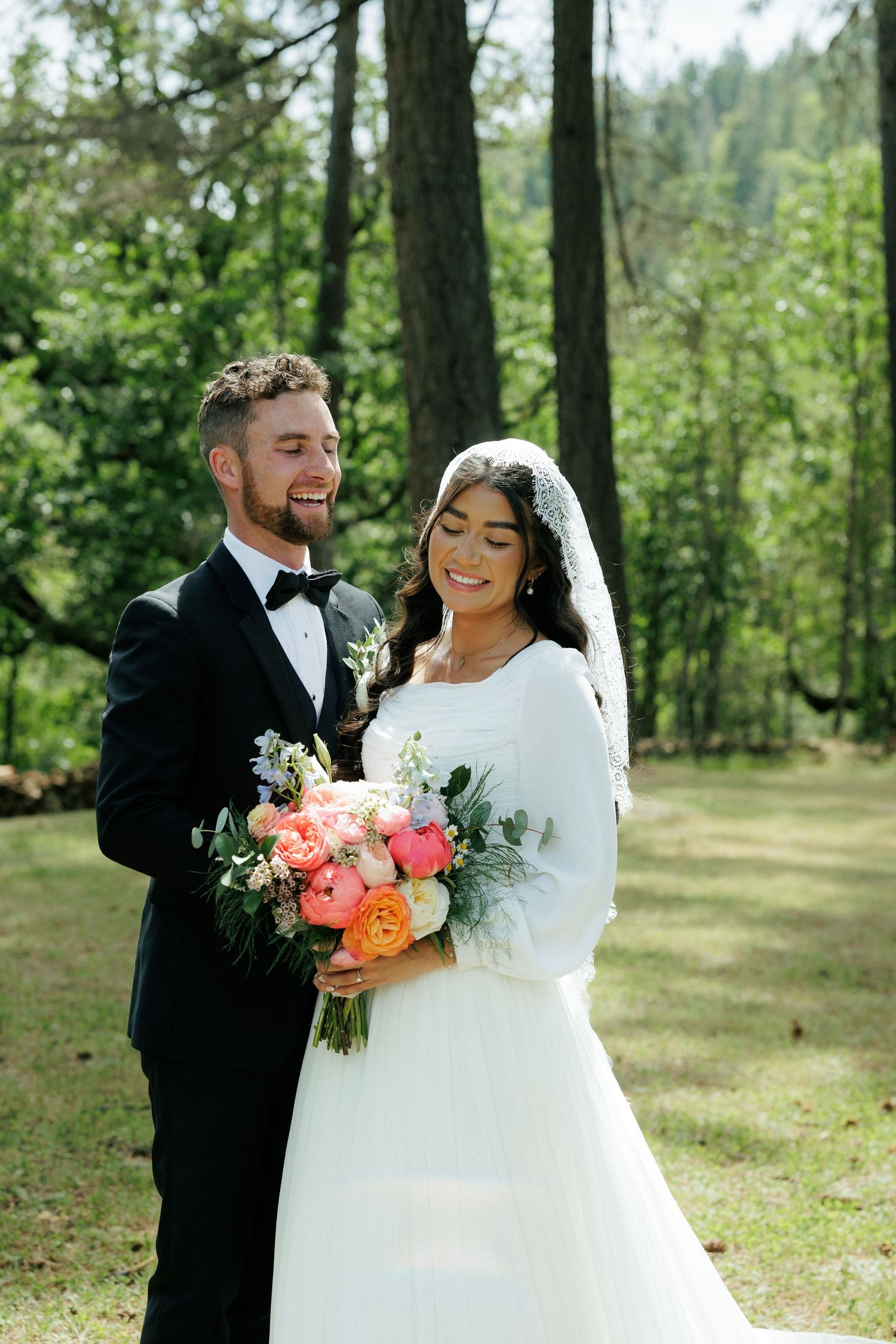 Newlyweds pose in forest with colorful bouquet during outdoor wedding.