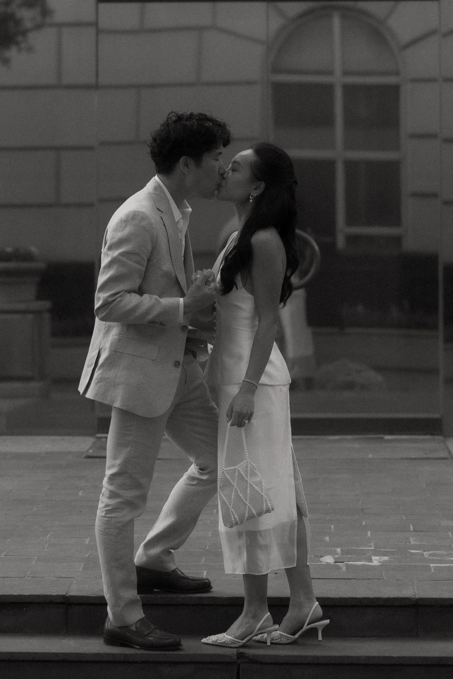 A romantic black and white photograph of a couple sharing a tender kiss outdoors near an elegant building.