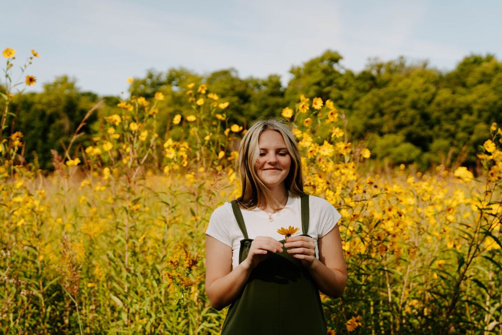 Person in overalls stands among vibrant yellow wildflowers on sunny summer day.