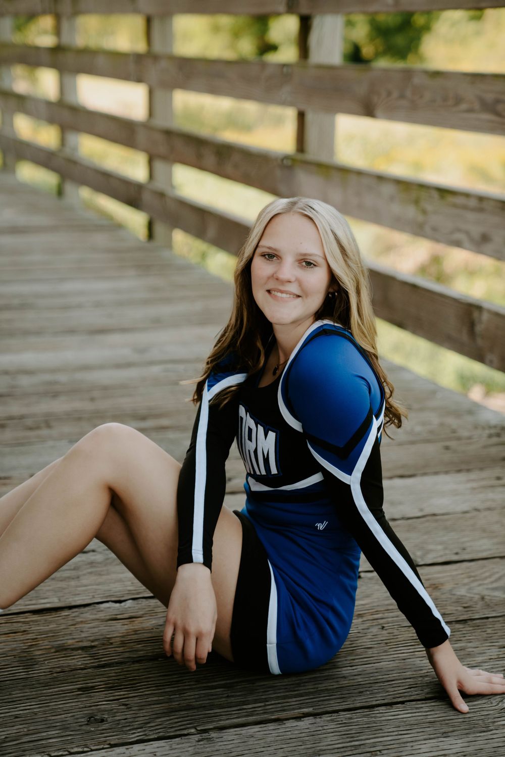 Athletic person in blue uniform poses casually on wooden deck.
