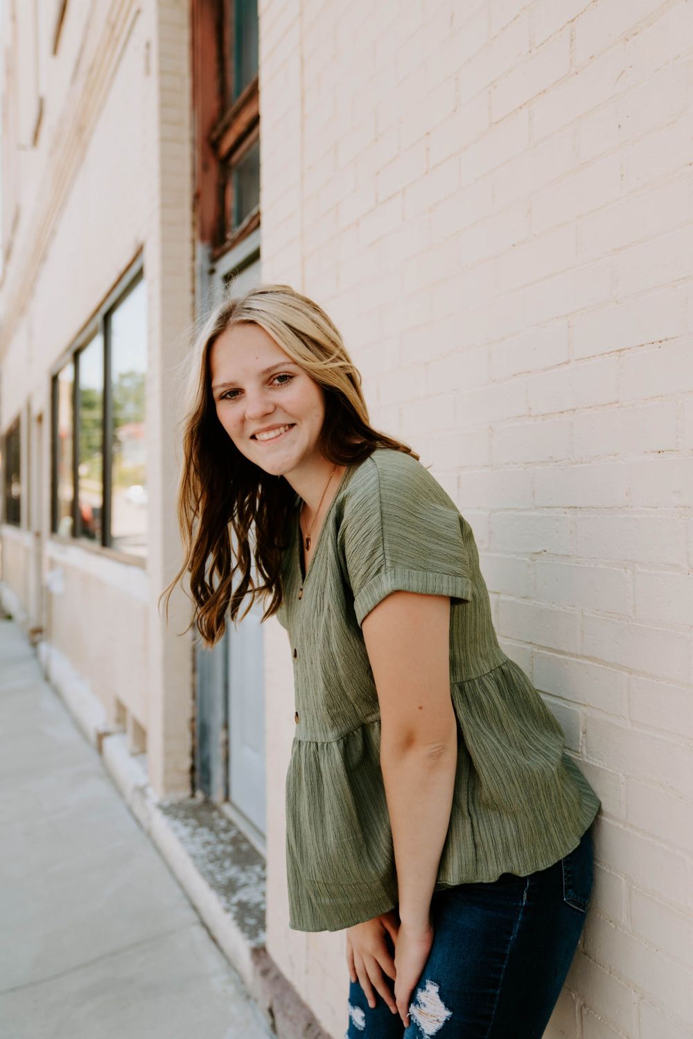 Casual portrait series featuring a sage green top and natural lighting against a white wall.