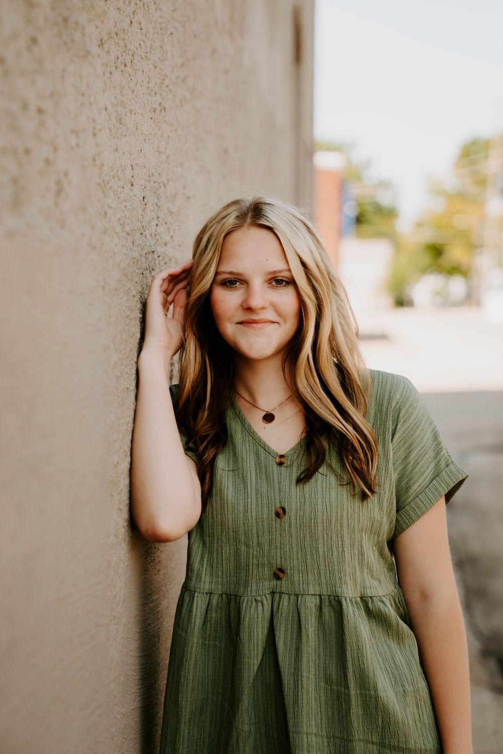 Multiple shots of someone in an olive green button-up dress against a concrete wall.