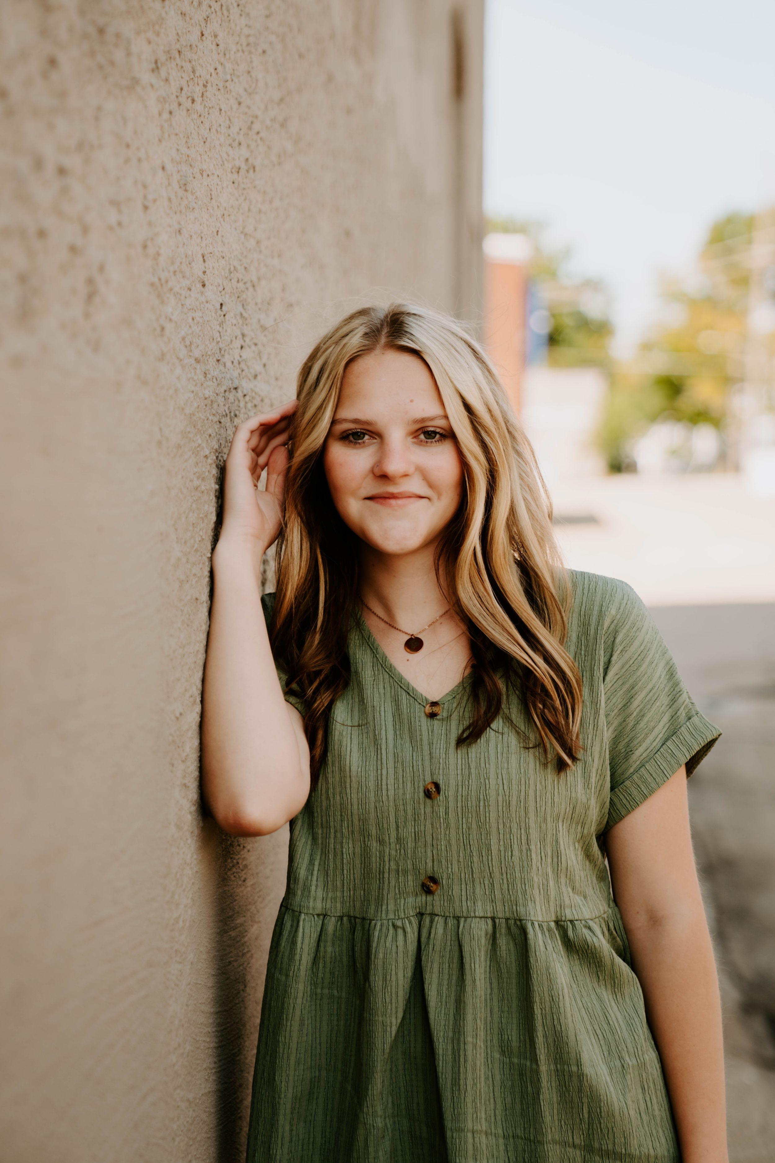 Multiple shots of someone in an olive green button-up dress against a concrete wall.