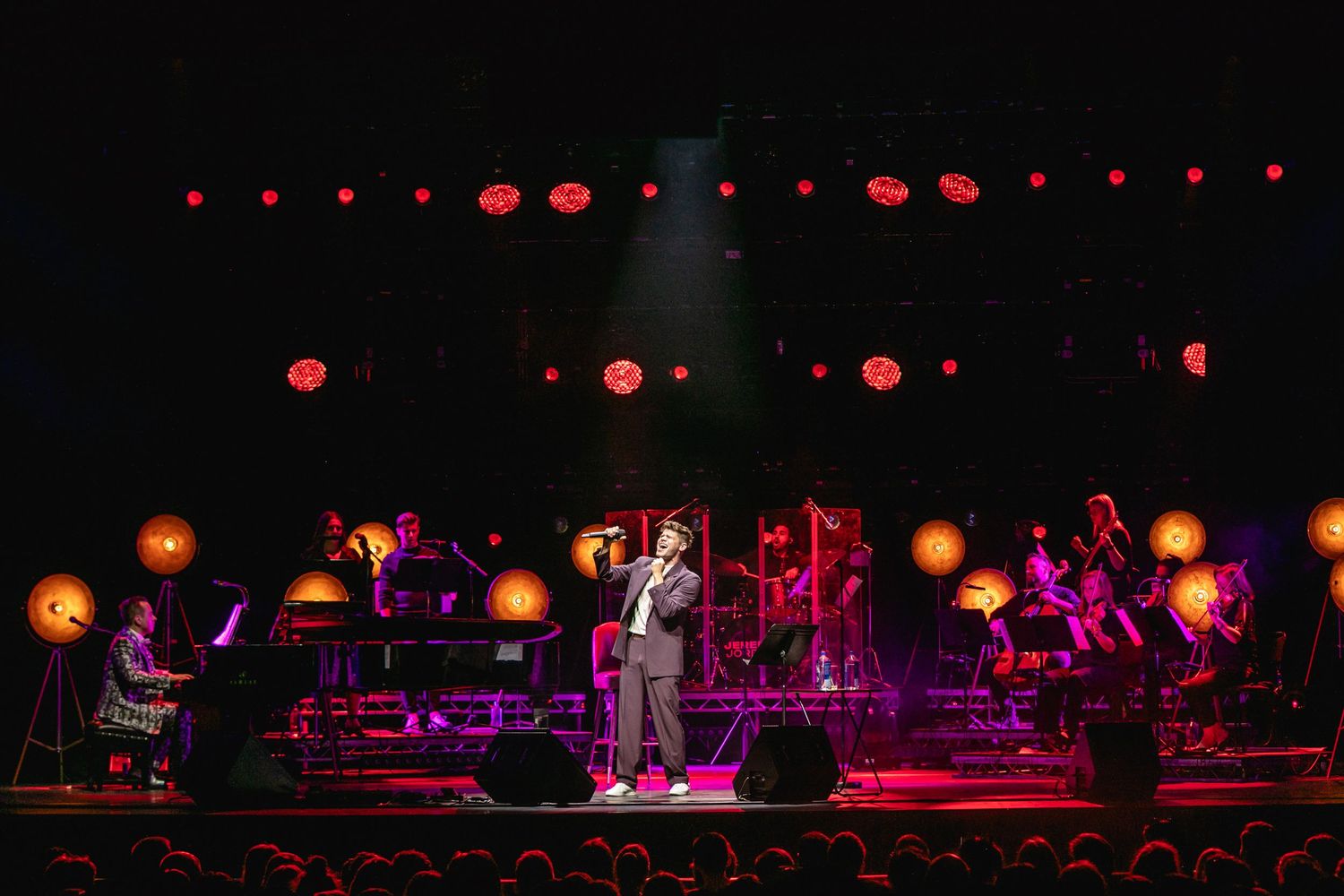 Concert performers on stage with dramatic red lighting and glowing orbs in the background.