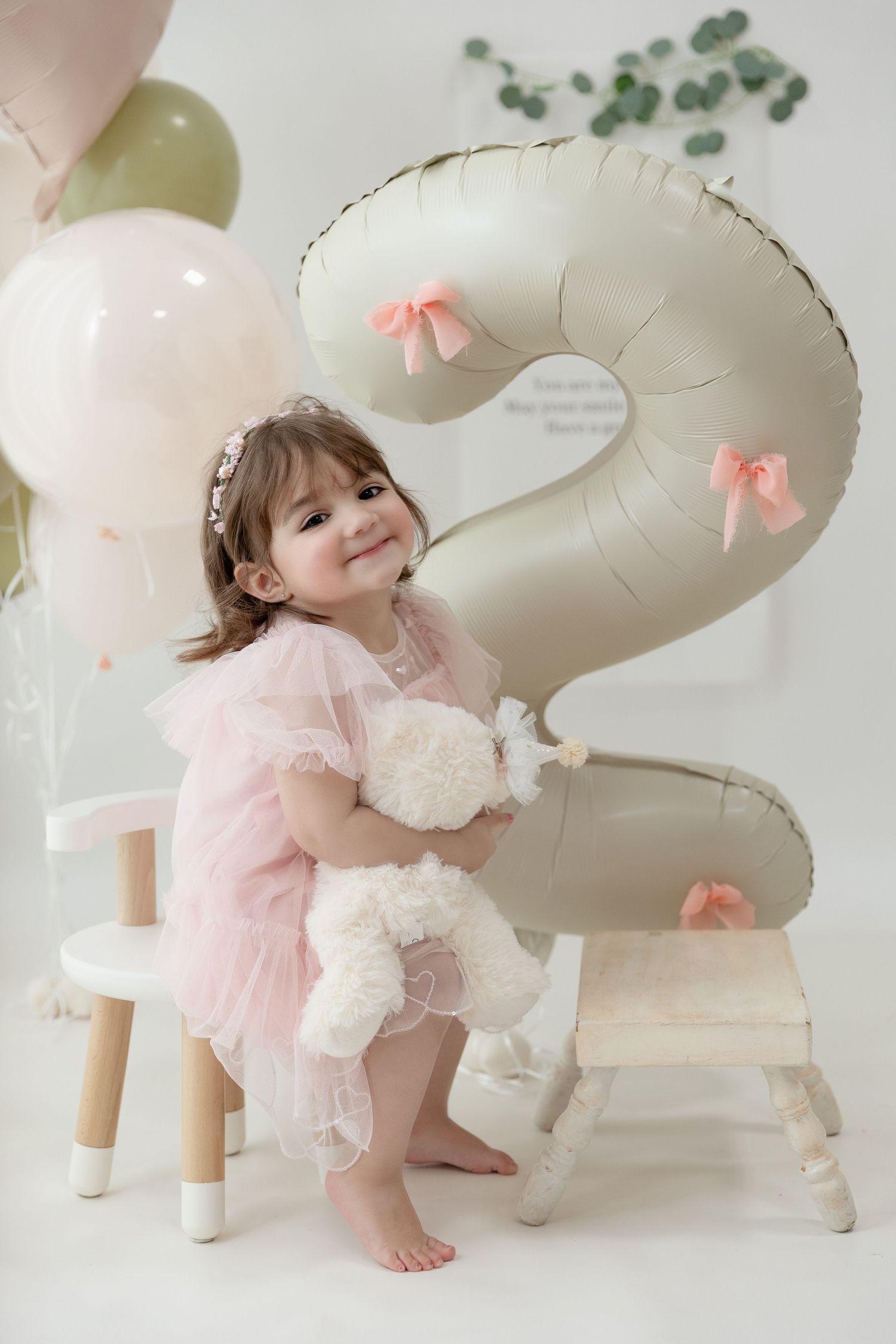Dreamy birthday setup with big number 2 balloon, soft balloons, and delicate pink dress against white background.