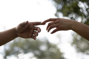 Two hands reaching towards each other against a blurred outdoor background in a recreation of Michelangelo's Creation of Adam.