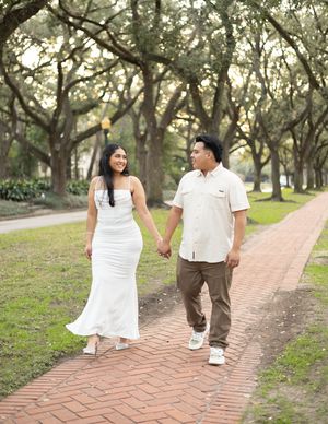 Couple walking hand in hand along a scenic brick pathway under beautiful moss-draped oak trees.
