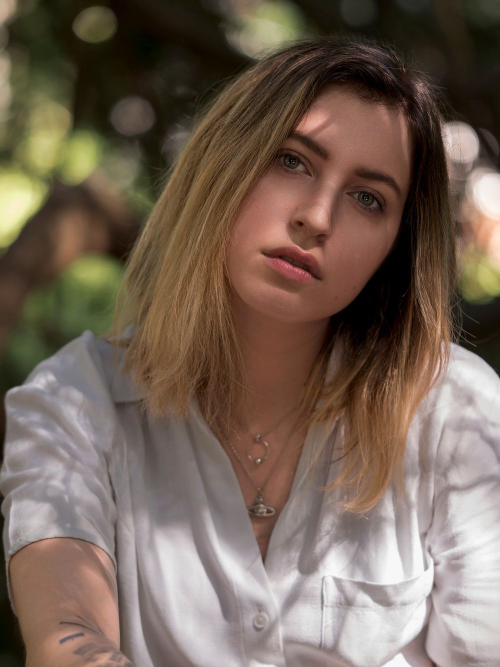 Portrait of someone with blonde hair wearing a white button-up shirt in natural outdoor lighting.