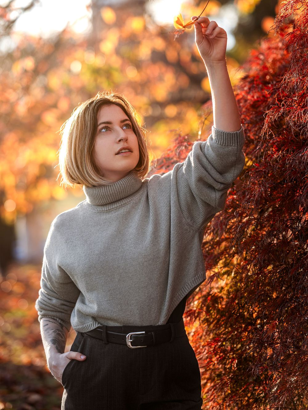 Someone wearing a cozy gray turtleneck sweater poses against vibrant autumn foliage in warm golden sunlight.