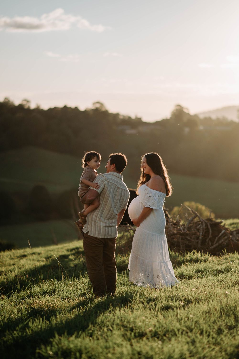 A family poses together at sunset in a grassy field with rolling hills in the background.