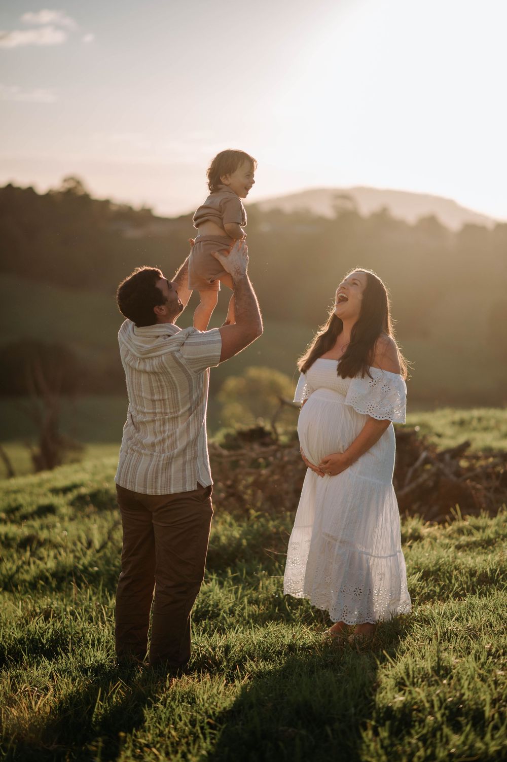 A scenic sunset photo of a family enjoying time together on a grassy hillside during golden hour.