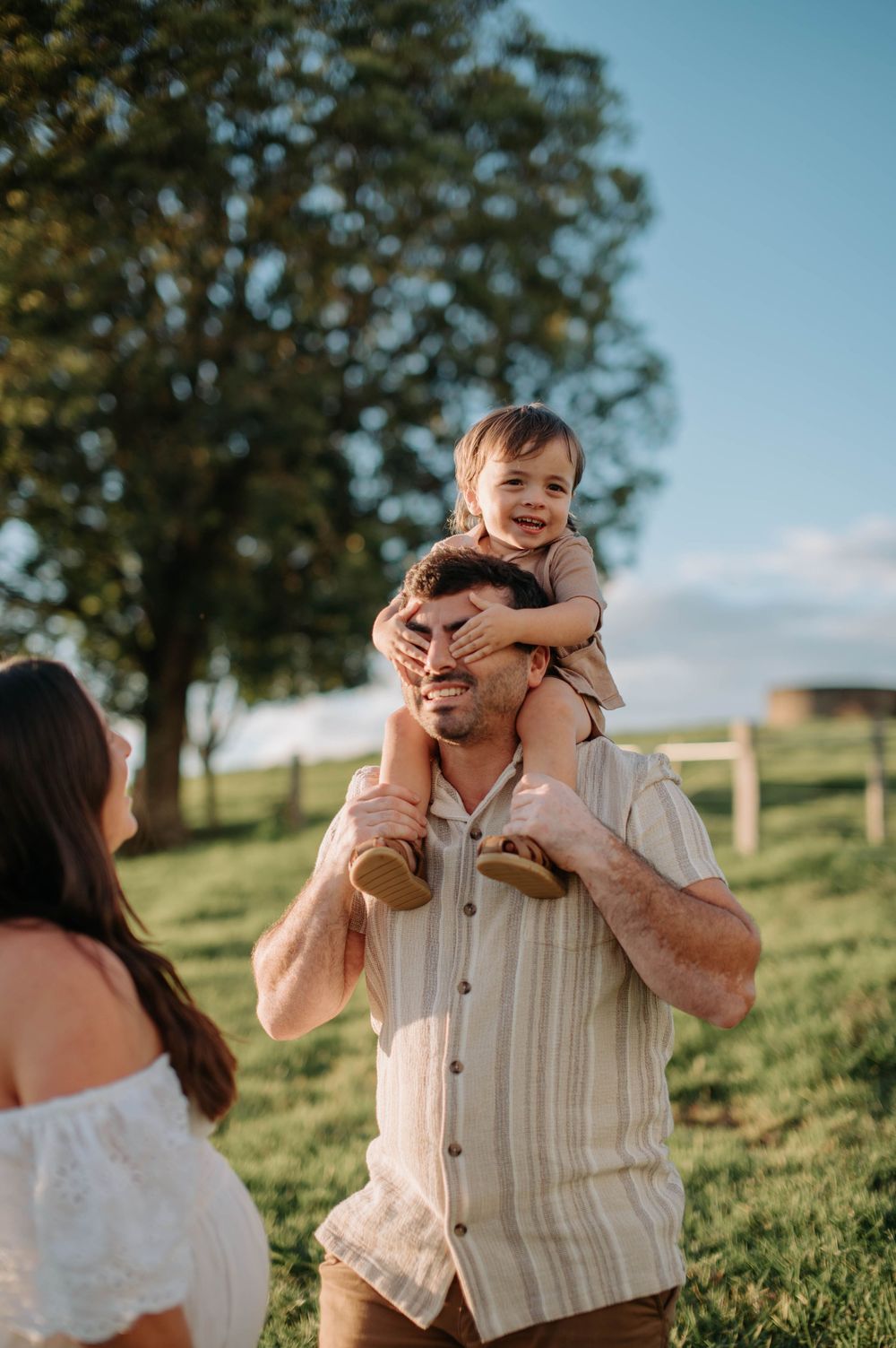 A joyful family moment captured outdoors on a sunny day with trees and rolling hills in the background.