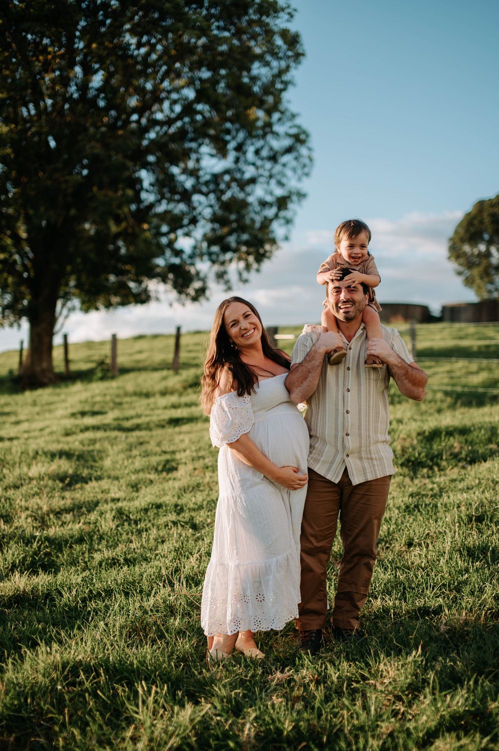 Expectant couple poses together in a scenic field with trees during golden hour photography session.