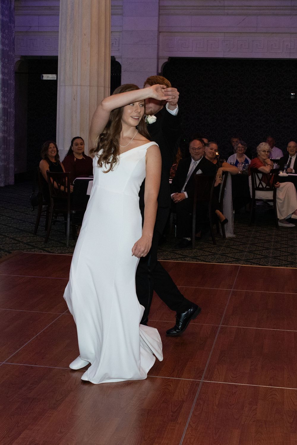 A couple performs an intimate slow dance on a polished wooden dance floor at their wedding reception.