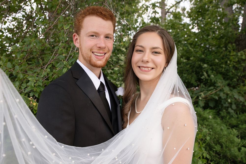 A wedding couple poses together outdoors in front of lush green foliage on their special day.