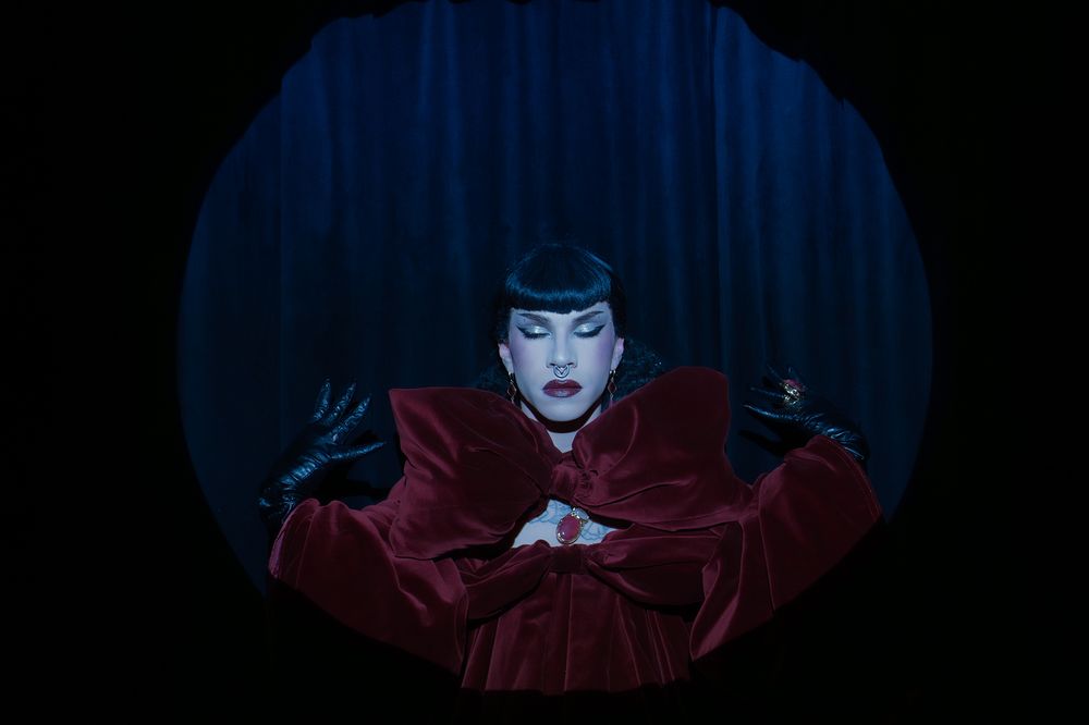 Theatrical performance with dramatic lighting and red velvet curtains.
