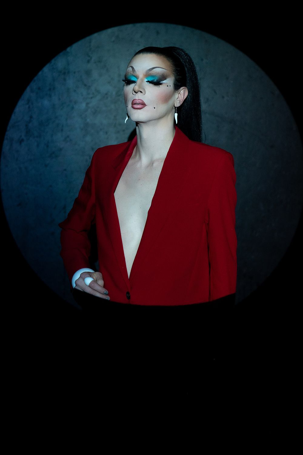 Fashion portrait against dark background featuring dramatic makeup and a red blazer with moody lighting.