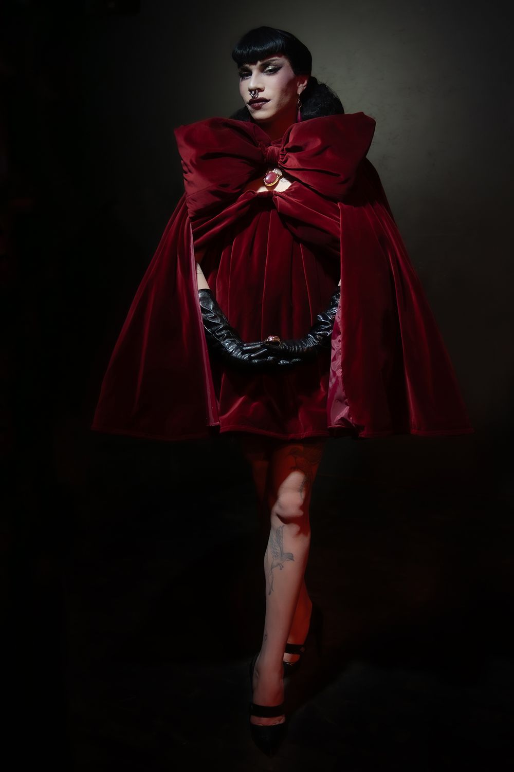 Dramatic fashion photo featuring deep red velvet cape against dark background.