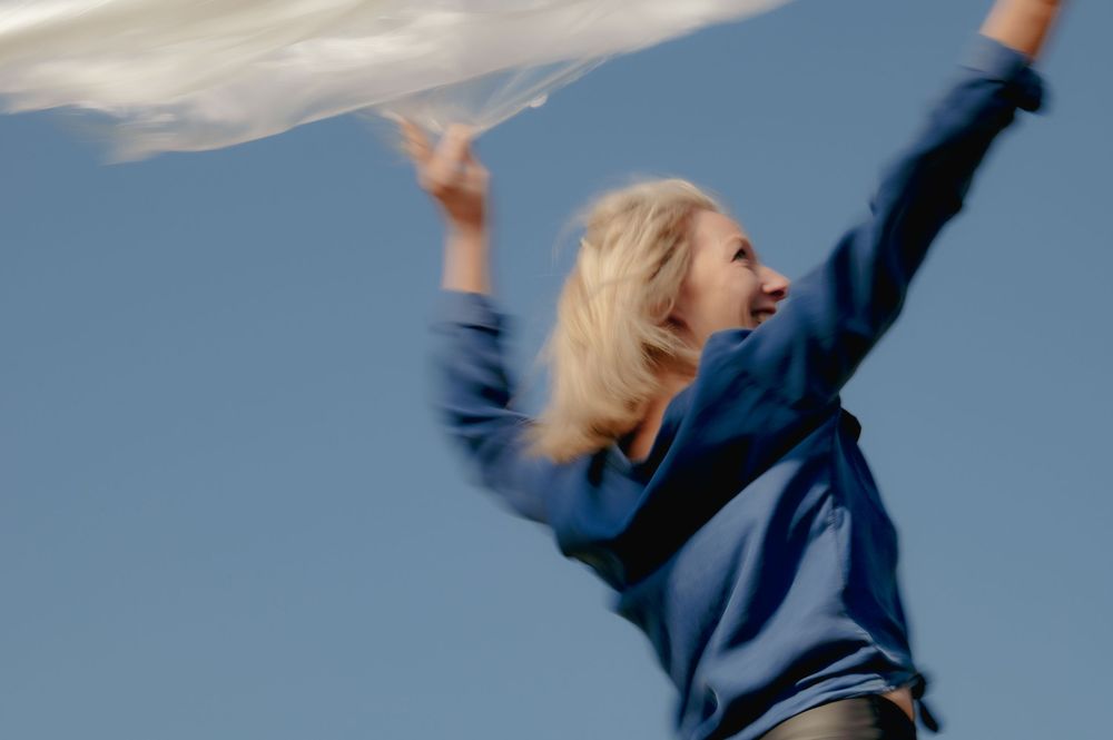 Person in blue jumping with arms spread against a bright sky.