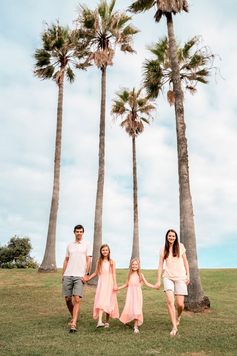 Family walking down toward a photographer with stunning palm trees in the background in the Freshwater park in the Northern Beaches