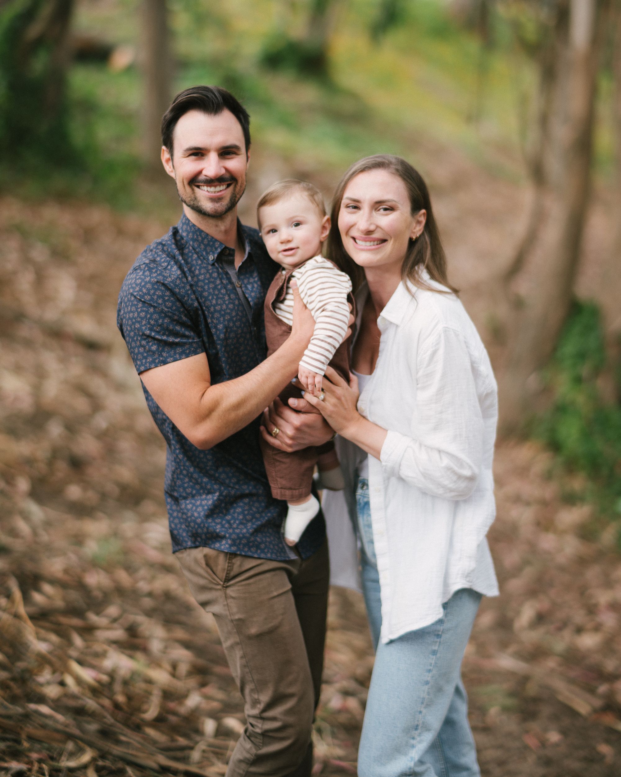 Family enjoying playful outdoor moment together among trees and natural setting.