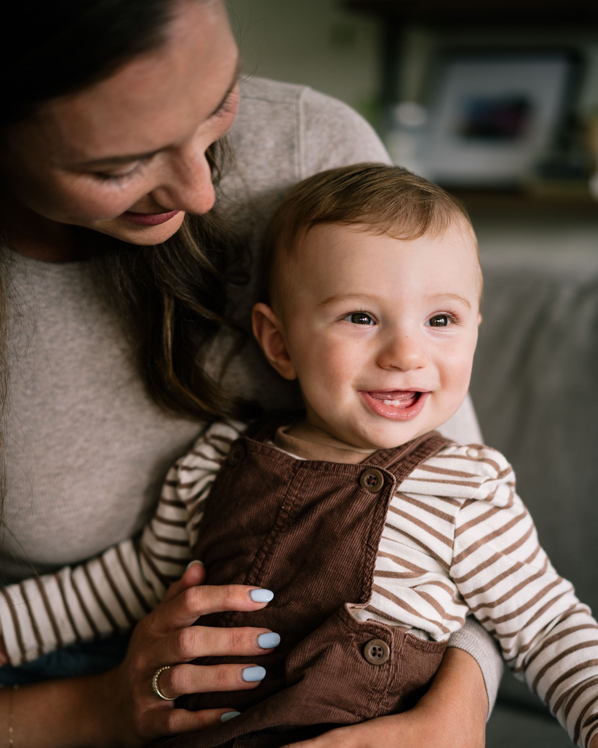 Baby in brown overalls and striped shirt smiling while adult hands support them.