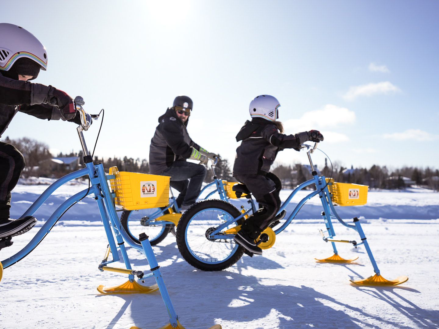 Snow bike riders performing stunts and tricks on a bright winter day.