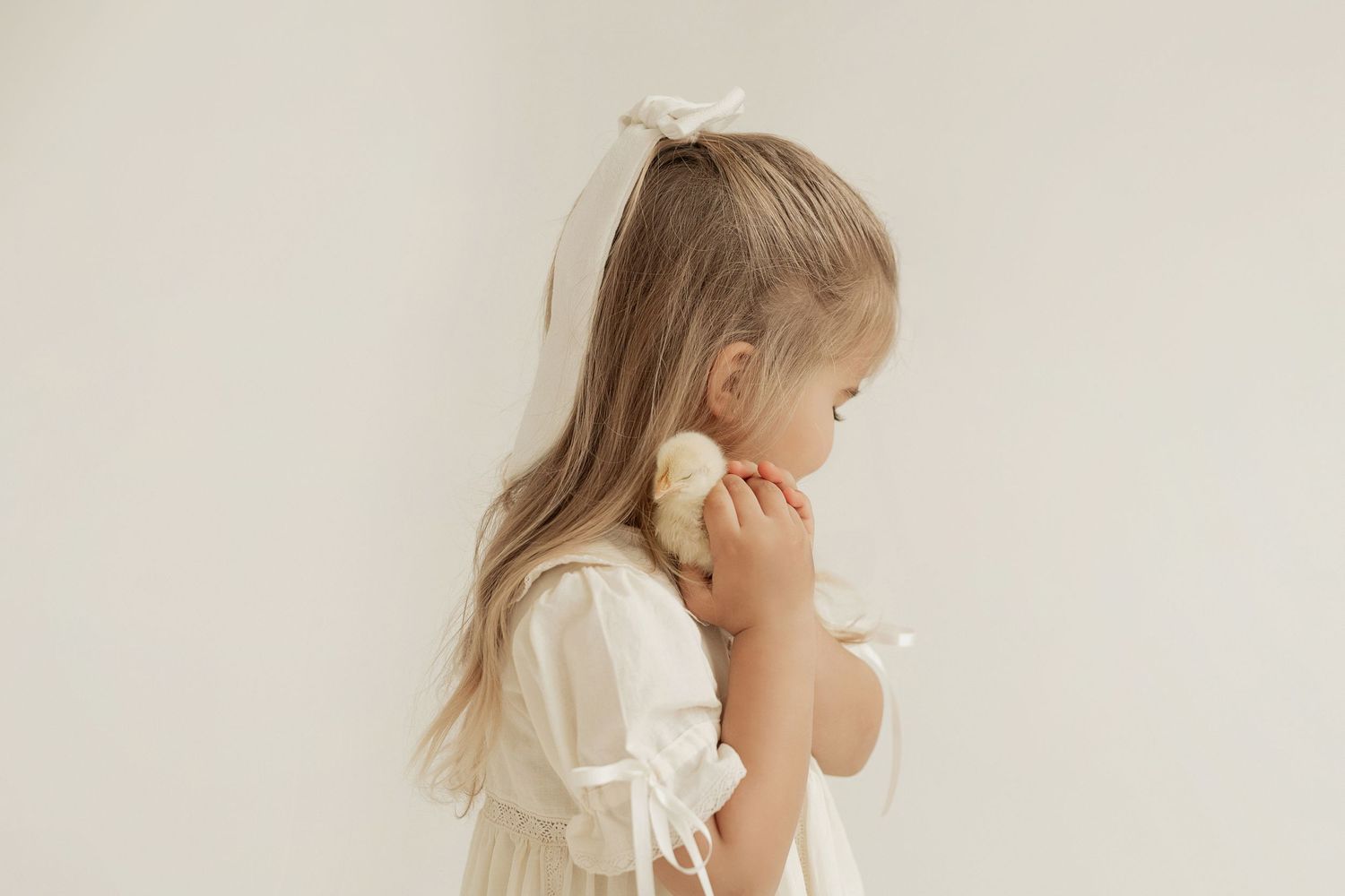 Child in white dress praying with hands clasped in a peaceful minimalist setting.