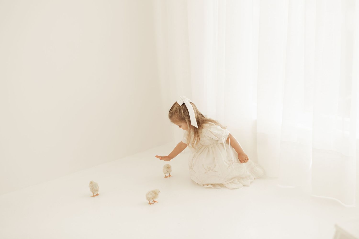 Small figure in white dress playing on floor in bright minimalist white room.