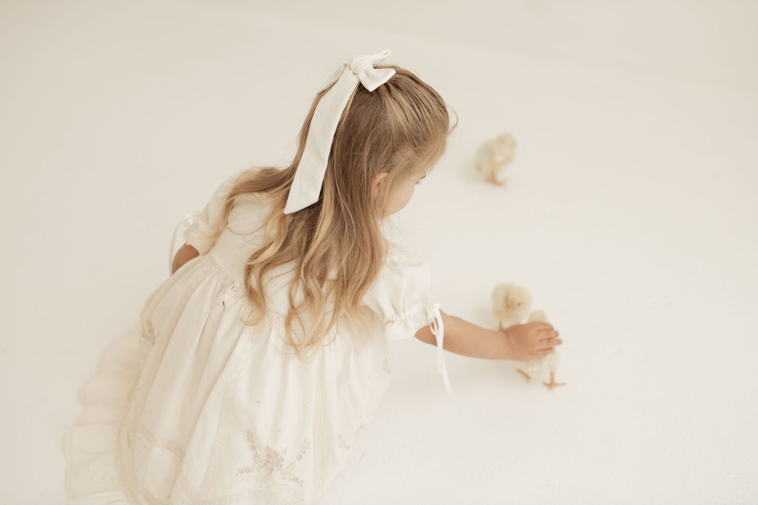 A dreamy ethereal scene with a person wearing a white dress and bow ribbon in their hair against a light background.