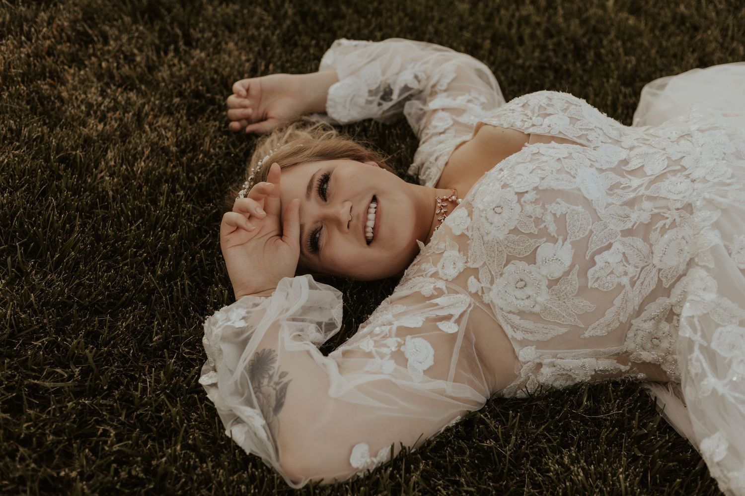A lace wedding dress detail as someone lays on grass in warm sunlight.