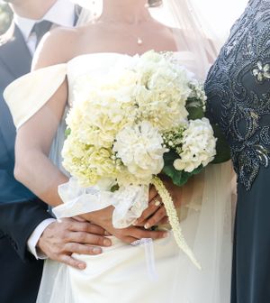 Bride holding elegant white hydrangea bouquet wrapped in lace ribbon at wedding ceremony.