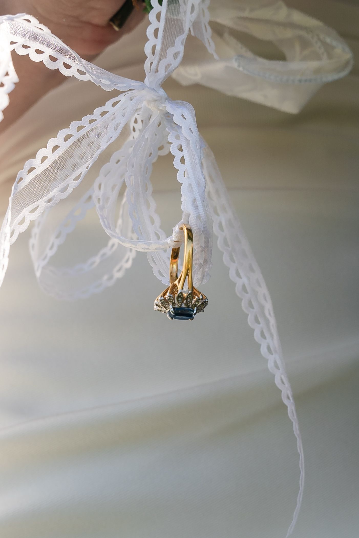 Gold wedding rings with blue sapphire tied to white lace ribbon bow detail.
