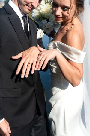 Newlyweds displaying wedding rings on their hands after ceremony, bride in off-shoulder white gown.