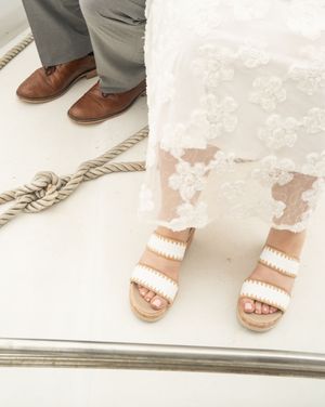 Close-up of a bride in white lace sandals and groom in brown leather shoes standing on a boat deck with rope.