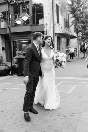 Black and white photo of smiling bride and groom walking together on city street.