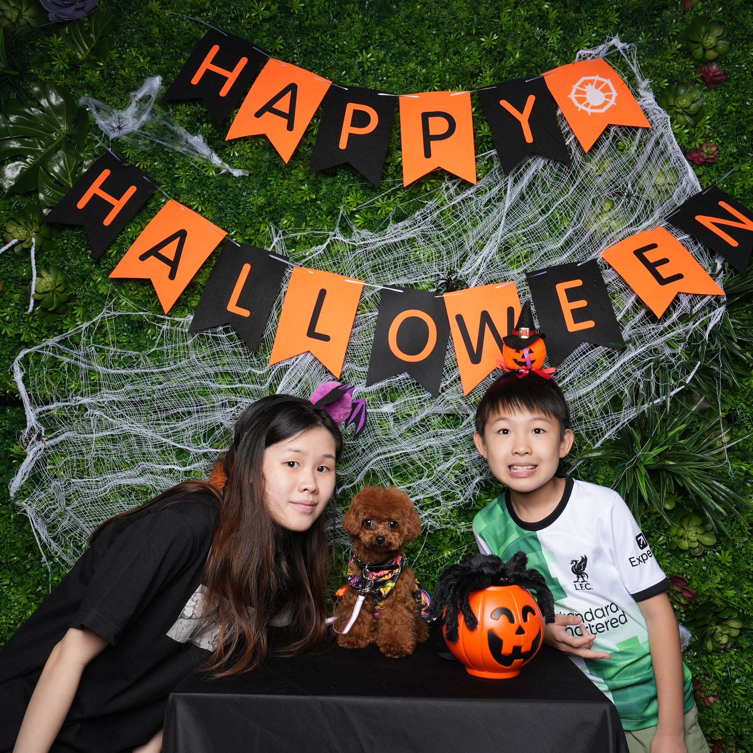 A festive Halloween scene with people posing by a Happy Halloween banner and spider web decorations.