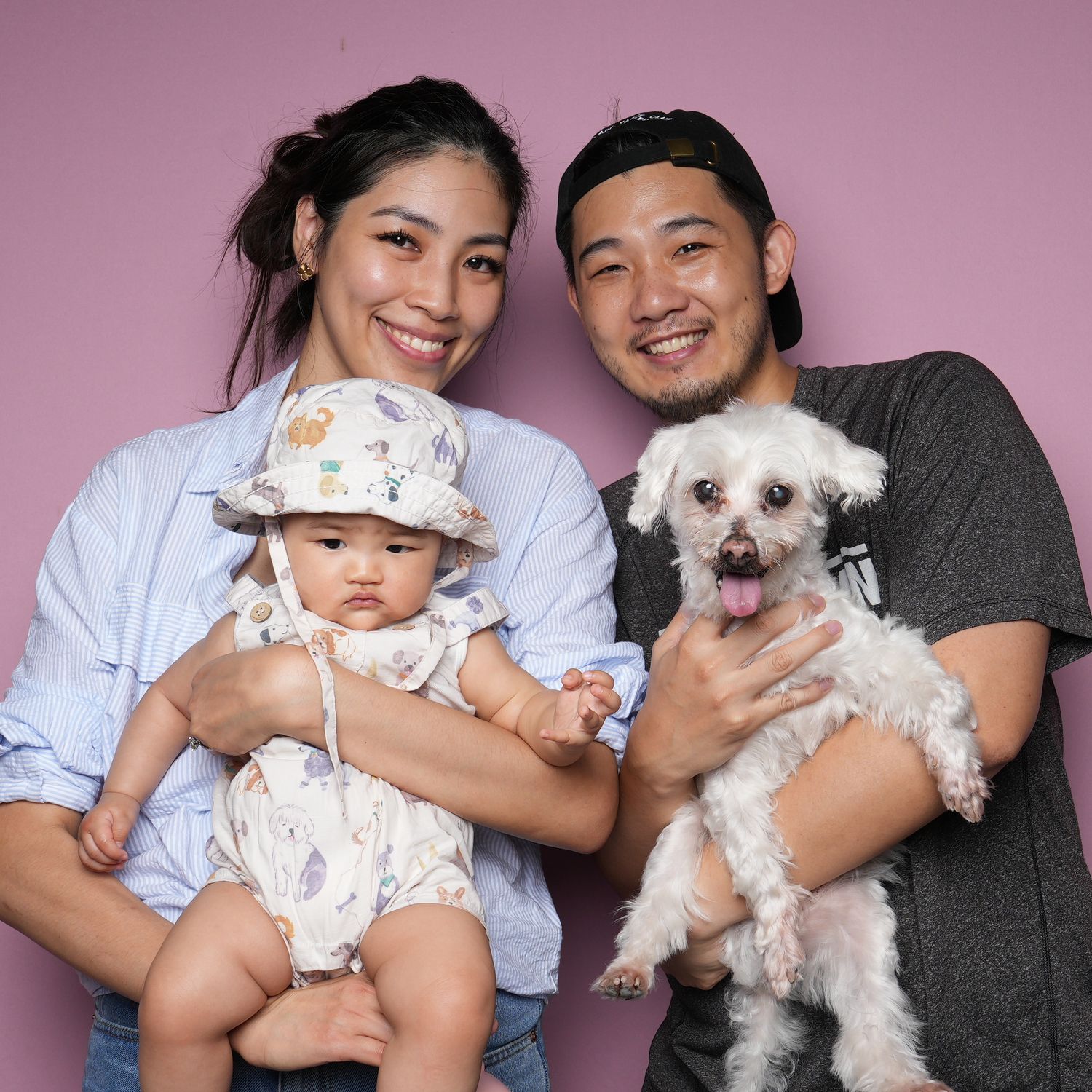 A family poses with their adorable white maltese dog against a pink background during a studio photoshoot.