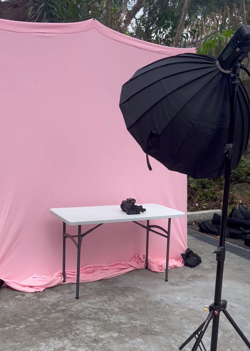 Photography studio setup with pink backdrop, white table, and black umbrella light modifier on a stand.