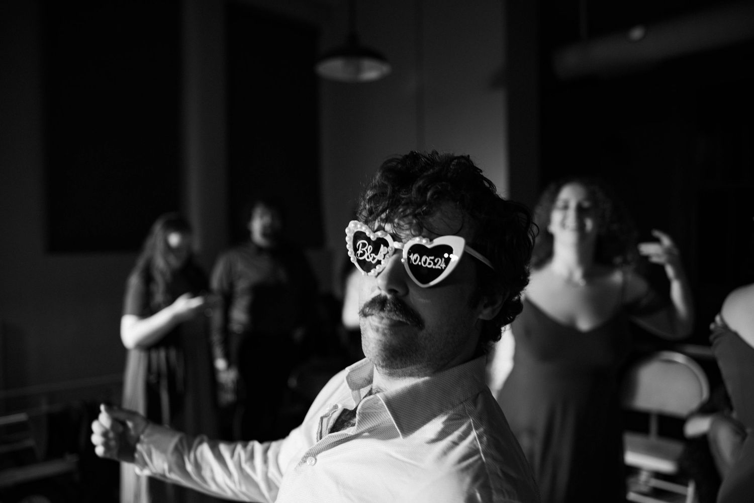 Person wearing heart-shaped sunglasses dancing in black and white.