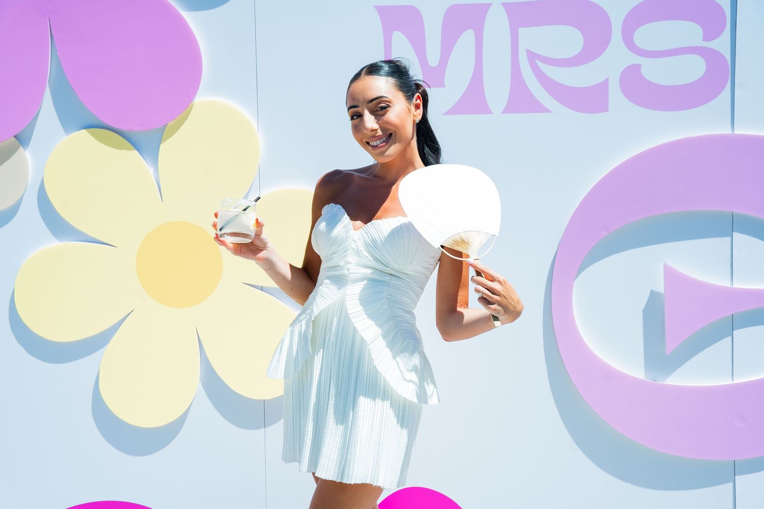 Woman in white dress posing with cotton candy against colorful flower backdrop.