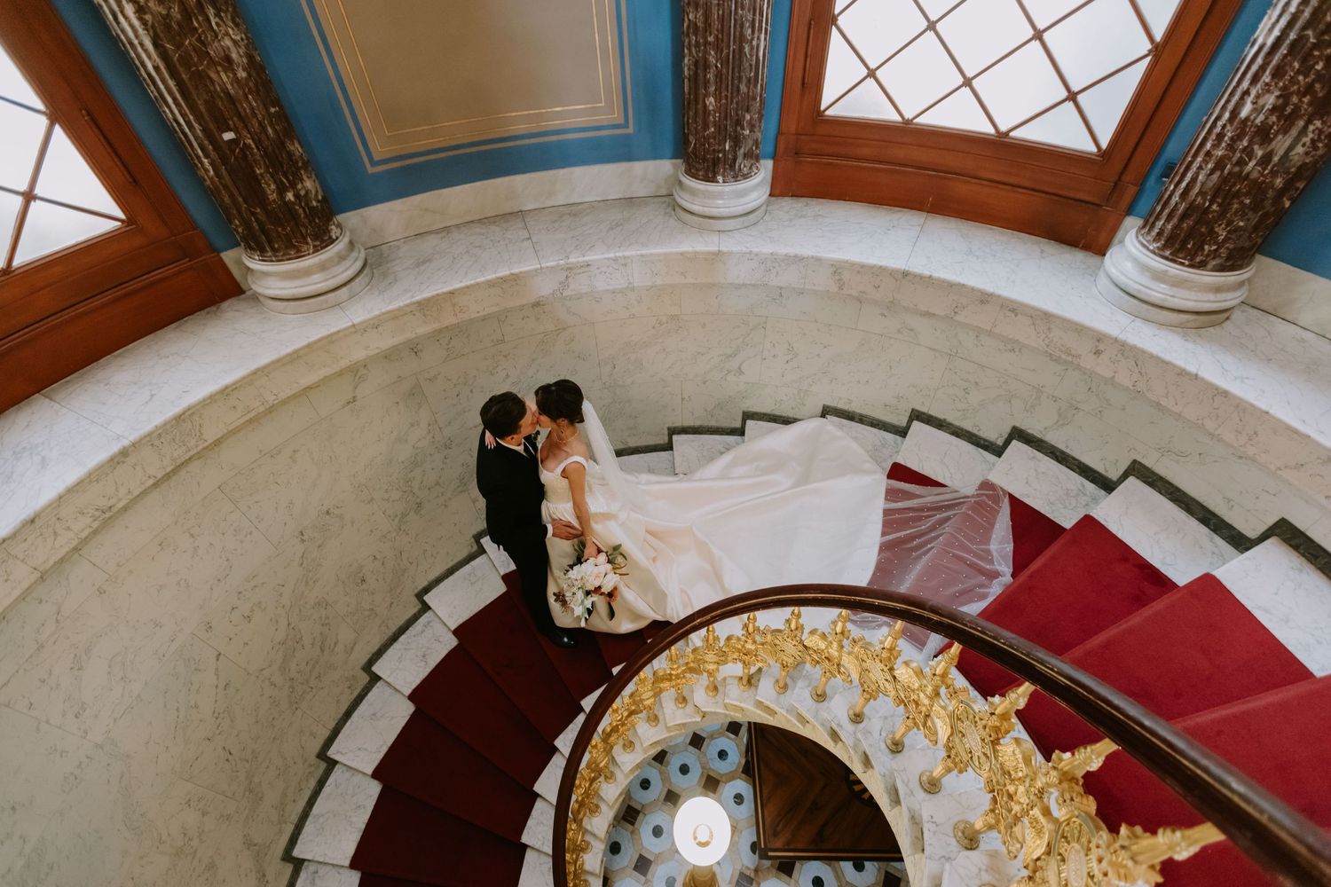 Couple captured from above on an elegant spiral staircase and red carpeting. Organized wedding by MyCastleWedding | Dresden.