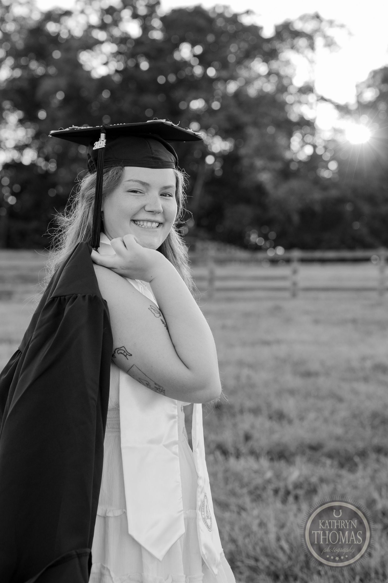 Black and white portrait of graduate in cap and gown with joyful expression outdoors.